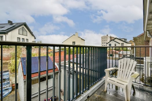 A picturesque urban balcony scene showcasing a plastic chair overlooking a neighborhood filled with rooftops and buildings under a cloudy sky.