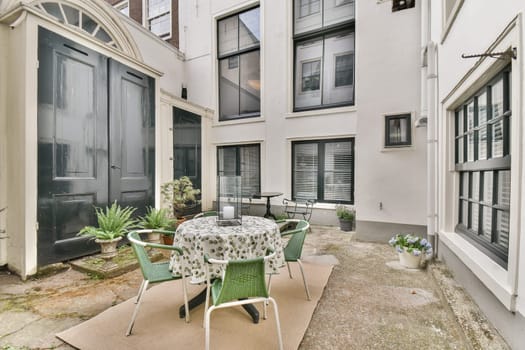 An inviting outdoor cafe area featuring a round table surrounded by green chairs, set against a backdrop of modern architectural elements and soft greenery.