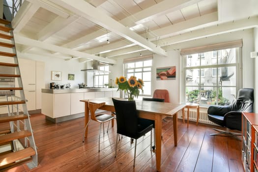 A chic modern interior featuring a wooden dining table, stylish chairs, and sunflowers, with an inviting atmosphere and natural light streaming through windows.