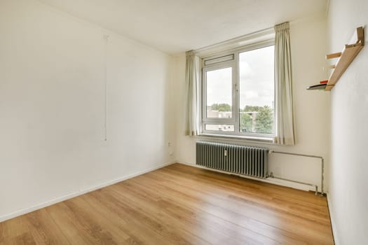 An uncluttered interior room featuring smooth wooden flooring, a large window allowing natural light, and minimal furnishings, perfect for modern living.