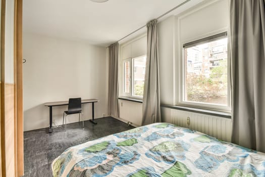 A bright, minimalist room featuring large windows, simple decor, and a colorful bedspread that enhances the tranquil atmosphere of the space.