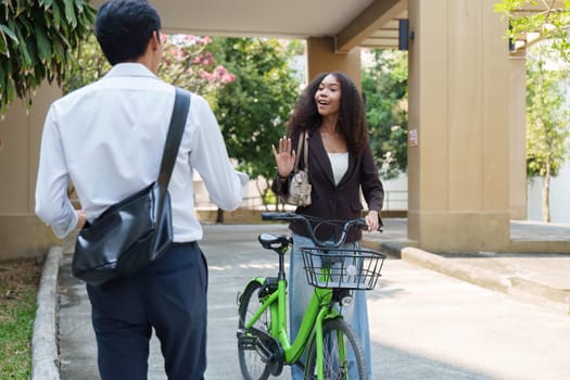 A young woman on a green bicycle greets her colleague with enthusiasm, highlighting the importance of using sustainable transport methods while promoting a healthy lifestyle.