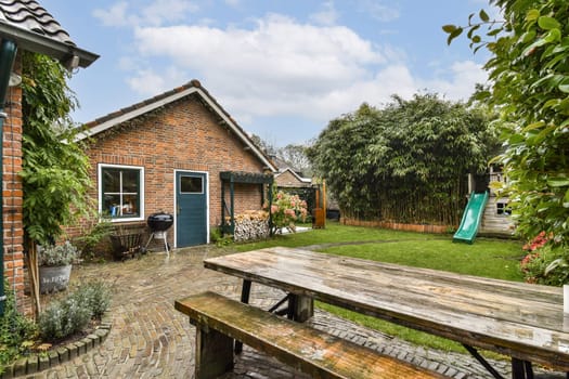 A cozy backyard showcases a beautifully manicured garden with vibrant plants, a wooden patio table, and a slide for children's fun, set against a serene sky.