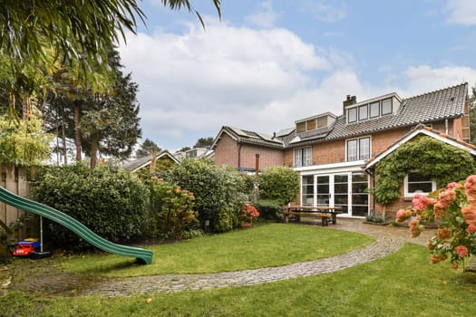A picturesque garden featuring lush greenery, a play slide, colorful flowers, and a cozy house, perfect for relaxation and outdoor activities.