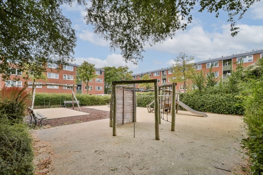 A serene urban playground features climbing structures and swings, nestled among lush greenery and modern residential buildings under a clear sky.
