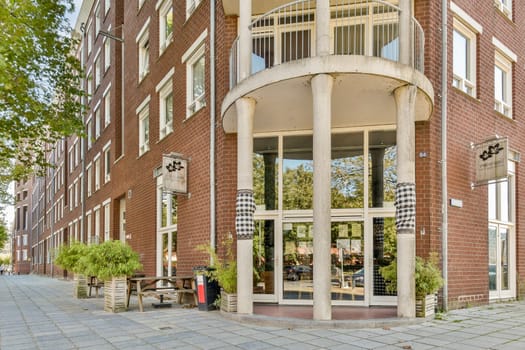 A striking modern building entrance featuring clean lines, large windows, and a stylish outdoor seating area, surrounded by lush greenery.