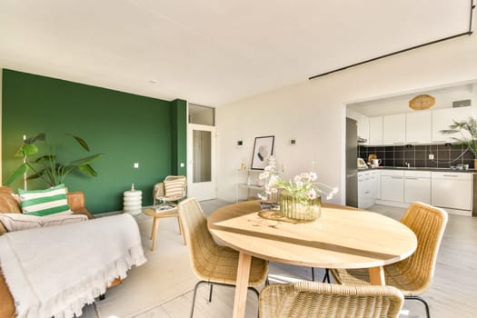 A chic living room featuring a green accent wall, cozy seating, and floral decor, seamlessly connected to a contemporary kitchen area.