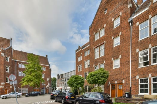 An inviting view showcasing red brick buildings with white accents, surrounded by greenery and parked cars in an urban environment.
