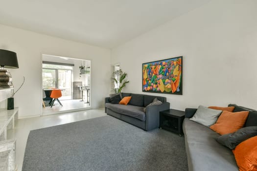 A stylish living room featuring a gray sofa, colorful wall art, and a bright orange chair, creating a vibrant and contemporary atmosphere.