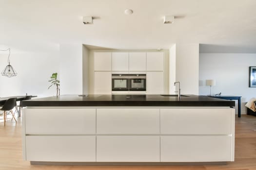 A sleek and contemporary kitchen featuring a large island with a dark countertop, white cabinetry, and ample natural light, exemplifying minimalist design principles.