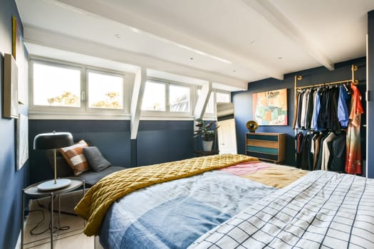 A contemporary bedroom showcasing a mix of textures and colors, featuring a cozy bed, stylish clothing rack, and beautiful natural light filtering through large windows.