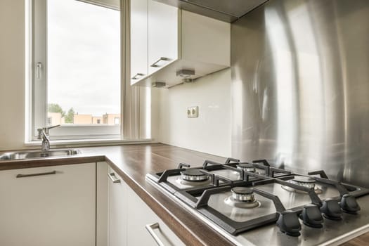 A sleek and contemporary kitchen design featuring a gas stove, cabinets, and a large window allowing natural light to flood the space.