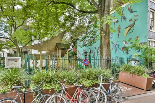 A vibrant urban park scene featuring lush greenery, a unique mural on the building, and parked bicycles creating a lively outdoor atmosphere.