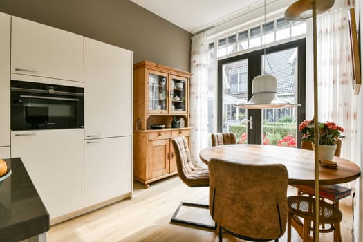 A stylish modern kitchen featuring sleek cabinetry, warm wood accents, and ample natural light streaming through large windows adorned with curtains.