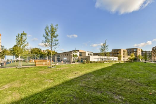 A vibrant urban park features lush grass, well-maintained trees, and a playground, showcasing a serene environment amidst contemporary architecture.
