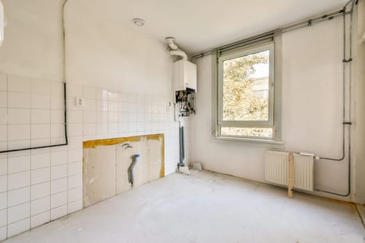 A vacant room showcasing white walls and utilities such as a window, radiator, and plumbing fixtures, awaiting completion.