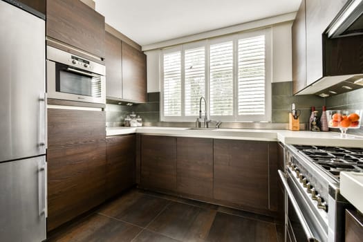 A sleek modern kitchen featuring wooden cabinetry, stainless steel appliances, and ample natural light from large windows, creating an inviting cooking space.