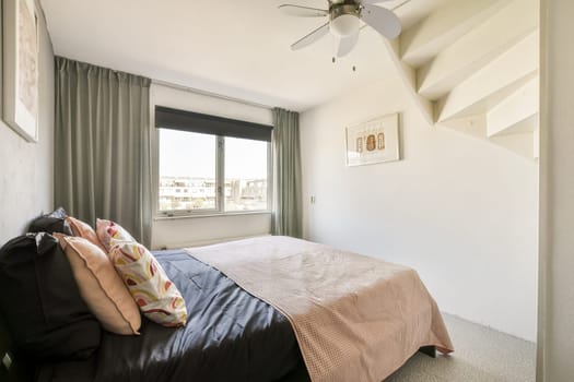 A stylish and contemporary bedroom featuring a bed with decorative pillows, large window with curtains, and modern design elements.