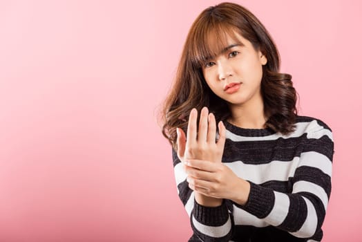 Portrait of Asian beautiful young woman suffering from pain in palm or hands and massaging her painful hands, studio shot isolated on pink background, Health care arthritis concept, Wrist pain