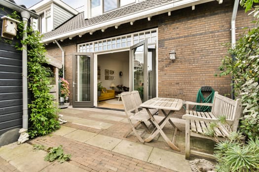 A cozy outdoor patio featuring wooden furniture and a brick wall of a contemporary house, adorned with greenery and inviting decor.