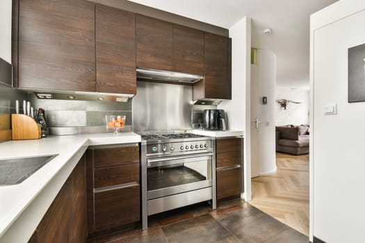 A sleek and contemporary kitchen design featuring dark wooden cabinets, stainless steel appliances, and an open layout that connects to a living area.