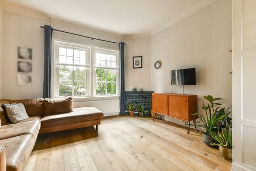 A beautifully designed living room featuring a comfortable sofa, wooden flooring, and large windows that invite natural light, enhancing the inviting atmosphere.