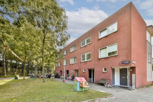 A contemporary residential building showcasing a red brick facade, surrounded by greenery and playground equipment, ideal for family living.