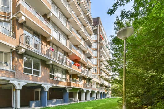 A modern residential building featuring balconies, large windows, and vibrant flower pots, set against a backdrop of lush greenery and trees.