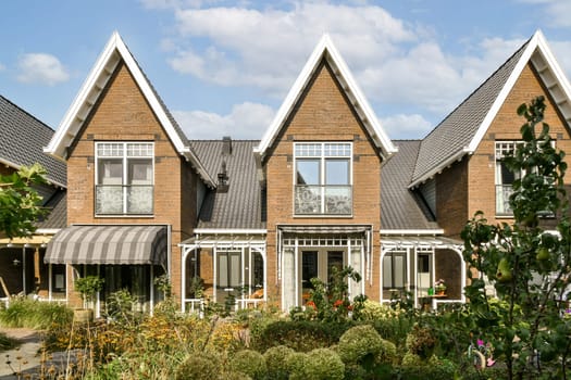 A row of contemporary townhouses showcases unique architecture with charming details. Lush greenery and colorful flowers enhance the inviting atmosphere.