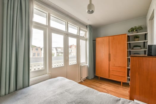 A serene bedroom featuring large windows that allow natural light to illuminate the space, complemented by wooden furniture and soft fabrics.