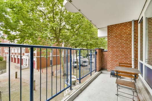A serene balcony view featuring a wooden table and chairs, surrounded by leafy trees and a peaceful neighborhood street with parked cars.
