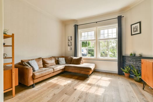 A contemporary living room featuring a brown leather sofa, large windows allowing natural light, and minimalistic decor to create a cozy atmosphere.