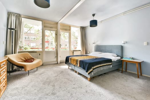 A contemporary bedroom featuring a comfy bed, stylish decor, and ample natural light from large windows. The room is designed with a serene color palette.