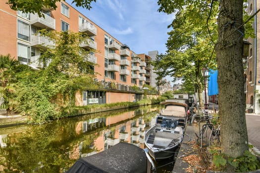 A picturesque canal scene showcasing modern buildings alongside lush greenery, with boats lined along the waterway, reflecting the architecture beautifully.