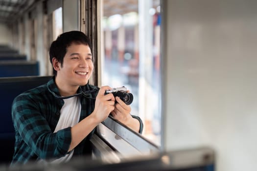 Enthusiastic about his journey, a young man holds a camera while gazing out the train window, ready to capture the scenic views.