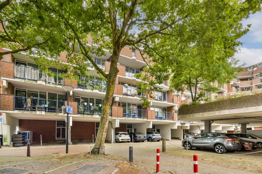 A contemporary urban residential building, characterized by a blend of greenery and architecture, showcasing parked cars and a vibrant neighborhood atmosphere.