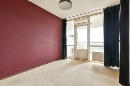 A serene interior showcasing a minimalist design with a burgundy accent wall, natural light streaming from the balcony, and soft textures on the floor.