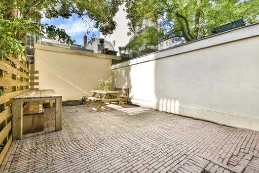 A serene outdoor patio featuring light brick flooring, wooden furniture, and lush greenery, perfect for relaxation and social gatherings.