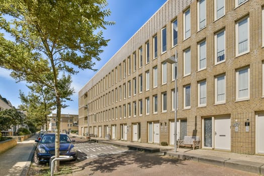 A striking modern building facade is framed by greenery and a pristine street. The architecture showcases large windows and a simplistic design.