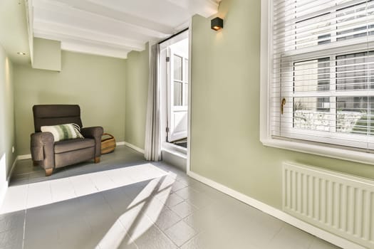 A bright and inviting interior featuring a comfortable chair, light green walls, and warm sunlight streaming through the window, creating a serene atmosphere.