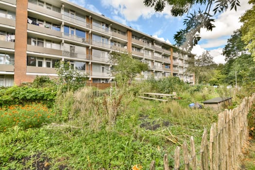 A vibrant urban garden featuring overgrown plants and flowers set against a backdrop of a modern apartment building. The setting highlights city living intertwined with nature.