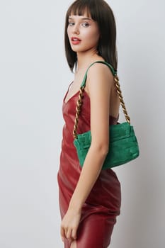 Young woman in a red dress holding a green handbag with a chain on her shoulder, isolated against a white background, showcasing fashion and style