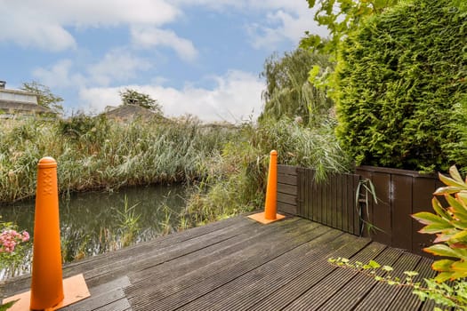 A serene view of a garden featuring dense greenery, wooden decking, and decorative orange cones, perfect for nature lovers and tranquil settings.