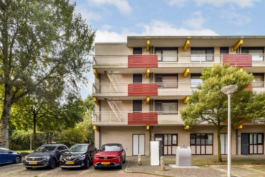 A contemporary apartment complex features balconies and is nestled among trees, providing a serene residential atmosphere. Cars are parked nearby.