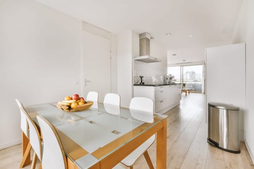 Contemporary minimalist style interior design of light studio apartment with wooden table and chairs in dining zone between open kitchen and living room with white walls and parquet floor