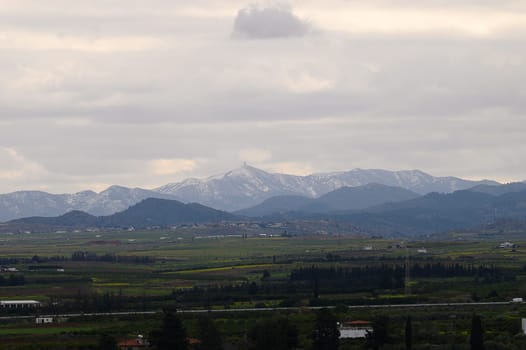 Majestic mountains loom in the background, partially shrouded in clouds, while a lush green landscape stretches below. The atmosphere is calm and serene, inviting reflection.