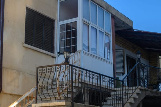 A two-story building stands proudly, featuring a glass-enclosed balcony that invites relaxation. The soft afternoon light casts a warm glow on the steps leading up, enhancing its charm.