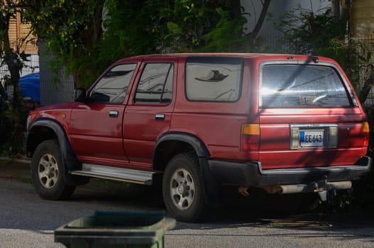 Under a bright sky, a striking red SUV rests beside an urban road, surrounded by greenery.