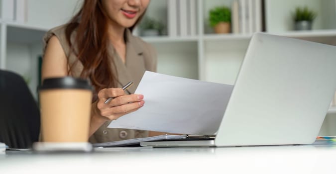 The woman holds papers in hand while reviewing her notes, exemplifying a proactive approach to her business tasks in a well-organized office environment.