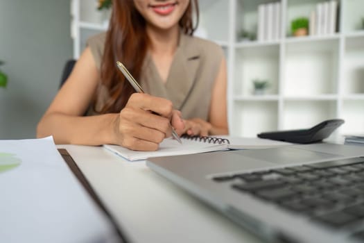 A determined professional writes down important information in a notebook while using her laptop, reflecting a productive work environment and active learning.